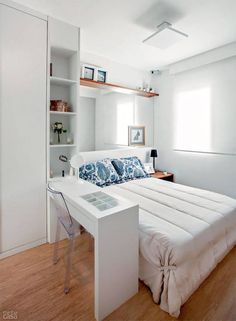 a white bed sitting under a window next to a book shelf filled with books on top of a hard wood floor