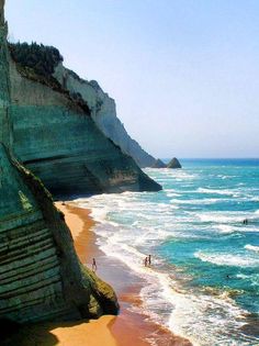 two people are walking along the beach by the water's edge with cliffs in the background