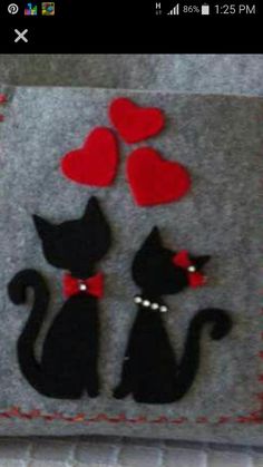 two black cats with red hearts sitting on a gray felt case that is attached to a pillow