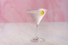 a martini glass with a lemon slice in it on a marble countertop next to a pink wall