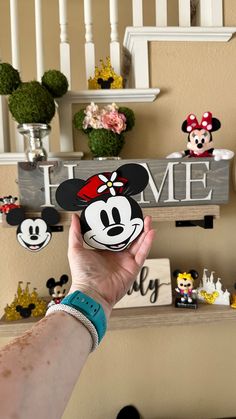 a person holding up a mickey mouse magnet in front of a wall with disney figurines on it