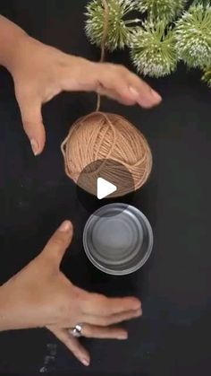 two hands reaching for a ball of yarn on top of a black surface with pine needles