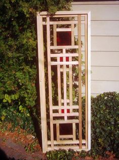 a wooden trellis in front of a house with bushes and shrubbery around it