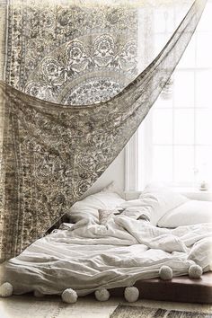 an unmade bed in front of a window with a mosquito net hanging over it