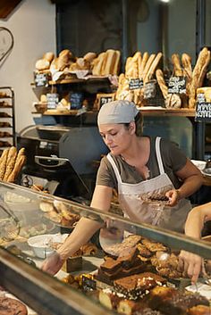 two women working in a bakery with lots of breads and pastries behind the counter