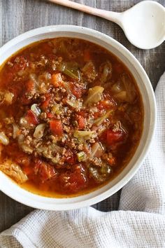 a white bowl filled with meat and vegetables next to a spoon on top of a table