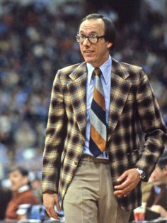 a man wearing a suit and tie standing in front of a crowd at a basketball game