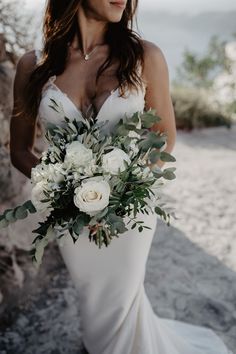 a woman wearing a wedding dress holding a bouquet of flowers and greenery in her hand