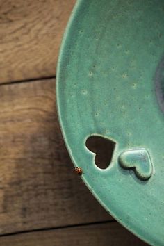 a green bowl with holes in the middle on a wooden table next to a wall