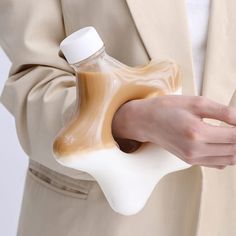 a person in a beige suit holding a white and brown bottle with liquid inside it