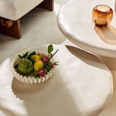 a bowl filled with fruit sitting on top of a white table next to a cup