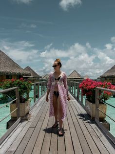 a woman walking across a wooden bridge next to flowers and thatched roof huts in the water