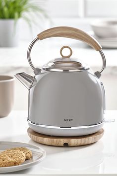 a silver tea kettle sitting on top of a counter next to a plate with cookies