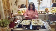 a woman standing in front of two trays of food on top of a stove