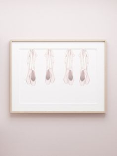 three ballet shoes hanging on the wall in front of a pink wall with a white frame