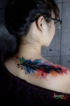 a woman's back shoulder with colorful ink splatters and an arrow tattoo