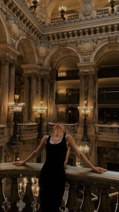 a woman in a black dress is standing on a balcony with chandeliers and lights