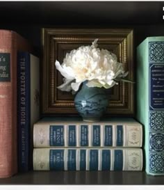 a shelf with books and a vase on it's top next to some flowers