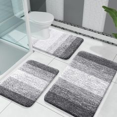 three bathroom rugs on the floor in front of a toilet