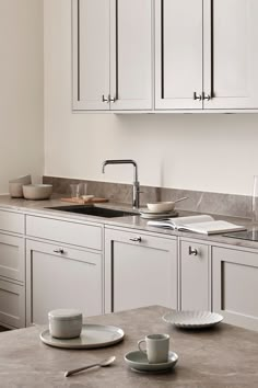 a kitchen with white cupboards and marble counter tops, two coffee cups on the table