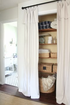 an open closet with white curtains and wicker baskets