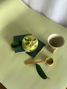 a table topped with a bowl of pickles and a spoon next to a cup