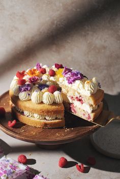 a cake with white frosting and colorful toppings on a wooden platter next to some raspberries