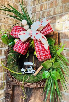 a wreath with red and white bows is hanging on a brick wall next to a potted plant