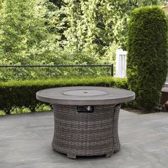 an outdoor table in the middle of a patio surrounded by hedges and bushes, with a bench to the side