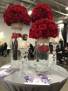 two vases with roses in them sitting on top of a round table at an event