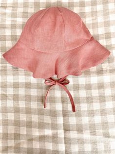 a pink hat on top of a checkered bed sheet with a red ribbon tied to it