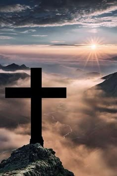 a cross on top of a mountain with the sun setting behind it and clouds below