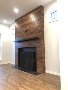 an empty living room with a fireplace and wood paneling on the wall, along with hard wood flooring