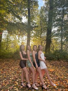 three young women posing for a photo in the woods with leaves on the ground and trees behind them