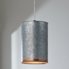 a light fixture hanging from a ceiling with a white wall in the background and sunlight coming through it