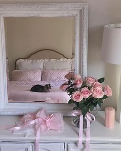 a cat laying on top of a white dresser next to a mirror