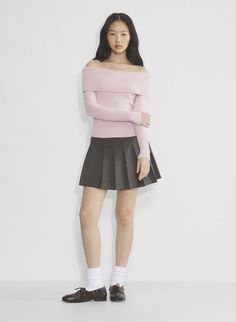 a woman standing in front of a white wall wearing a pink sweater and black skirt