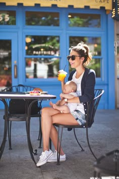 a woman holding a baby while sitting at a table with an ice cream sundae