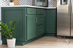 a kitchen with green cabinetry and stainless steel appliances in the corner, along with a potted plant