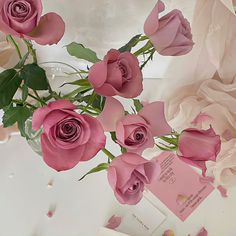 pink roses are arranged in a vase on a white surface with cards and confetti