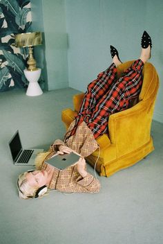 a woman laying on the floor with her legs up in an armchair while using a laptop computer