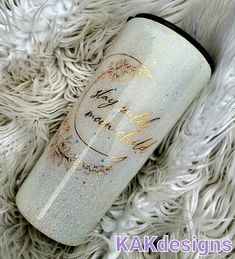 a white and gold glitter tumbler with writing on the side sitting on a furry surface