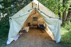 a tent set up in the woods with tables and chairs under it for people to sit outside