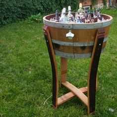 a wooden barrel with bottles in it sitting on the grass next to a fence and bushes