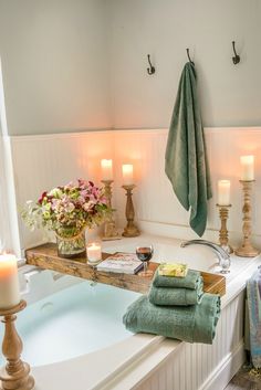 a bathroom with candles and towels on the bathtub next to the tub is filled with flowers