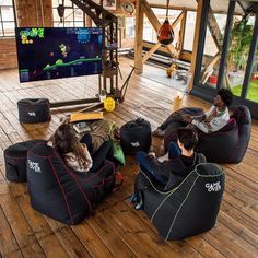 three people sitting on bean bag chairs in a room with wooden floors and large windows