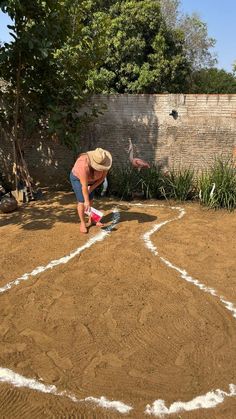 a man kneeling down on top of a dirt field next to a wall and trees