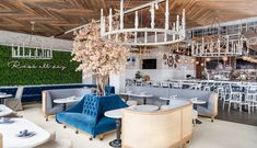 the interior of a restaurant with blue velvet chairs and white tables, chandeliers hanging from the ceiling