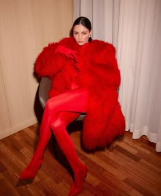 a woman in red is sitting on a chair with a fur coat over her shoulders