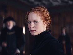 a woman with red hair and blue eyes in a black coat looking at the camera